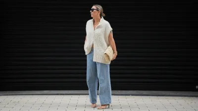 HAMBURG, GERMANY - SEPTEMBER 19: Aylin König is seen wearing a loose, chunky knit sleeveless, zip-up sweater in a soft beige tone with a wide collar and relaxed drape; light blue straight-leg jeans with a slightly wide fit; nude strappy heeled sandals; a beige woven-style clutch bag with a padded texture; stacked gold bracelets from Cartier; a watch with a metallic wristband and white clock face from Cartier; gold detailed rings; gold link earrings from Tiffany & Co HardWear Collection; black rectangular sunglasses; her dark hair is pulled back into a neat, low bun on September 19, 2025 in Hamburg, Germany. (Photo by Moritz Scholz/Getty Images)