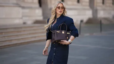 FRANKFURT AM MAIN, GERMANY - MAY 12: Paulina Kurka is seen wearing a navy blue cropped bomber jacket with big pockets from Zara, a denim midi dress with tailored waist and front button closure from Zara, light havana MU 04ZS sunglasses with round brown glasses and golden logo detail from Miu Miu, a chocolate brown Birkin 30 bag with golden details from Hermès, a silver triple wrap Farandole 120 fine link necklace with classic pendants from Hermès, silver hoop earrings, a medium sized silver Santos watch with square dial from Cartier, a silver Chaine d'ancre Enchainee chain bracelet from Hermès, a silver Chaine d'ancre Enchainee large model chain ring from Hermès, a custom-made diamond ring with square sapphire statement details, custom-made diamond engagement and wedding rings on May 12, 2025 in Frankfurt am Main, Germany. (Photo by Moritz Scholz/Getty Images)