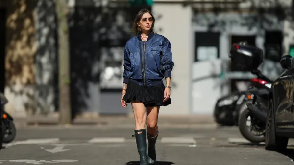 PARIS, FRANCE - SEPTEMBER 06: Emy Venturini wears straight light brown hair with a middle part, brown gradient sunglasses by Prada, gold hoop earrings by Rabanne, layered necklaces, multiple bracelets, a navy blue bomber jacket by Burberry, a short ruffled black dress by Zara Studio, and dark green rubber rain boots by Hunter, during a street style fashion photo session, on September 06, 2025 in Paris, France. (Photo by Edward Berthelot/Getty Images)