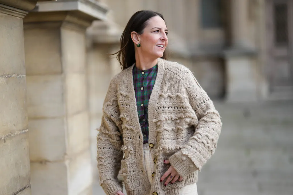 PARIS, FRANCE - MARCH 27: Alba Garavito Torre wears gold and green cross print pattern earrings, a green and purple checkered print pattern / puffy shoulder / buttoned shirt from Nina Blanc, high waist ivory high waist wide legs pants from Nina Blanc, a beige wool embroidered pattern oversized buttoned cardigan , during a street style fashion photo session, on March 27, 2023 in Paris, France. (Photo by Edward Berthelot/Getty Images)