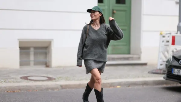 BERLIN, GERMANY - SEPTEMBER 16: Anna Schürrle seen wearing dark green Fulfilled baseball cap with white embroidered lettering at the front. Her hair is straight and left down, tucked behind her ears so the cap frames her face neatly. Her makeup is minimal and natural. Around her neck, she has a delicate gold tennis necklace, Soft Goat cozy oversized v-neck sweater in a soft, fuzzy grey knit. The relaxed fit, with slightly long sleeves, creates an effortless, slouchy silhouette, matching Soft Goat mini skirt, also in fuzzy grey knit. The skirt features an asymmetrical hemline, Chanel black 2.55 handbag, worn on the shoulder with the signature gold chain strap and Dorothee Schumacher cowboy boots in black leather. The boots feature detailed stitching along the shaft and silver metallic tips at the toes, on September 16, 2025 in Berlin, Germany. (Photo by Jeremy Moeller/Getty Images)