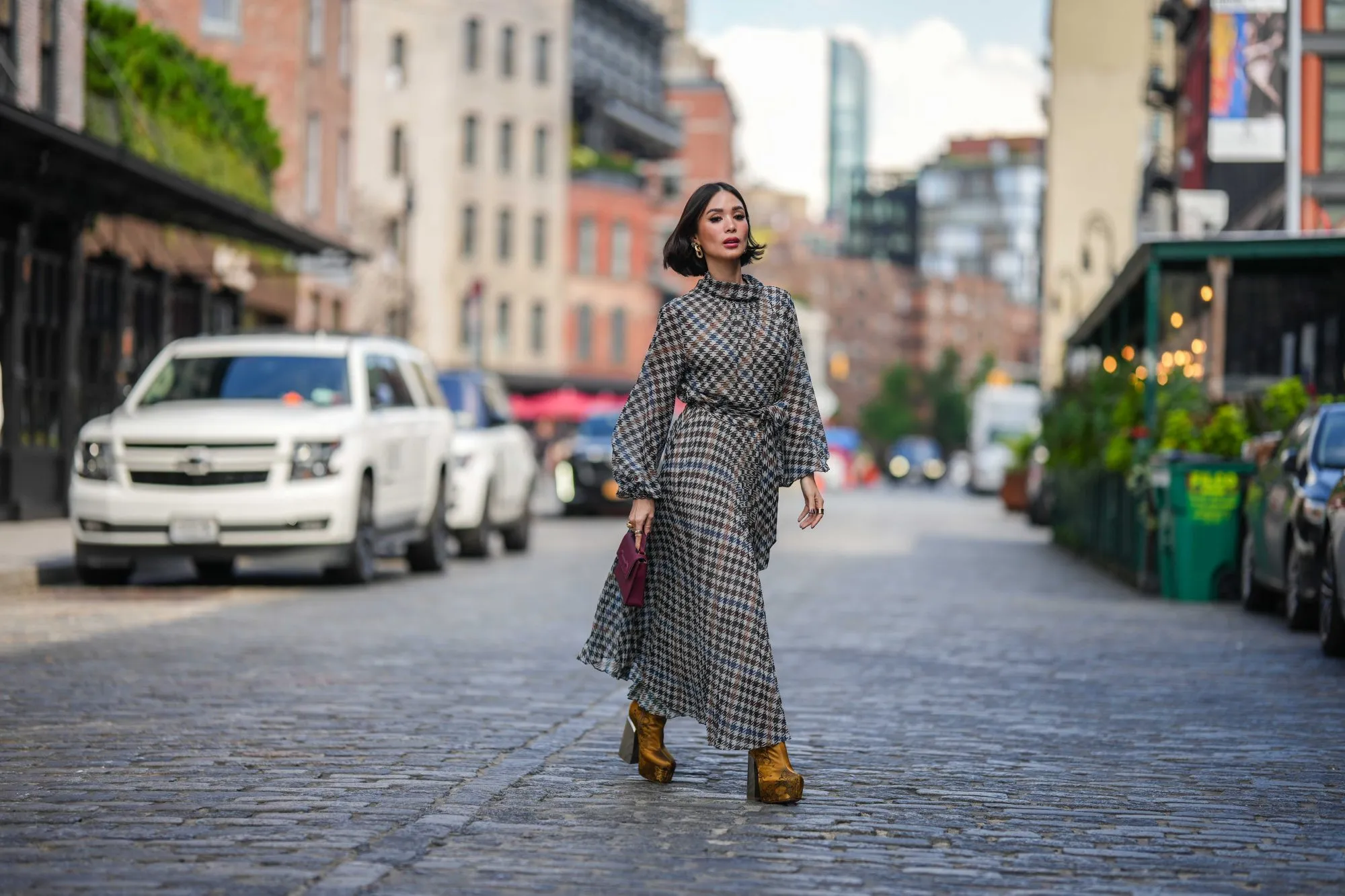 NEW YORK, NEW YORK - SEPTEMBER 12: Heart Evangelista wears golden earrings, a houndstooth pattern printed midi pleated dress, a burgundy leather bag from Carolina Herrera, golden floral print platform boots, outside Carolina Herrera, during New York Fashion Week, on September 12, 2023 in New York City. (Photo by Edward Berthelot/Getty Images)