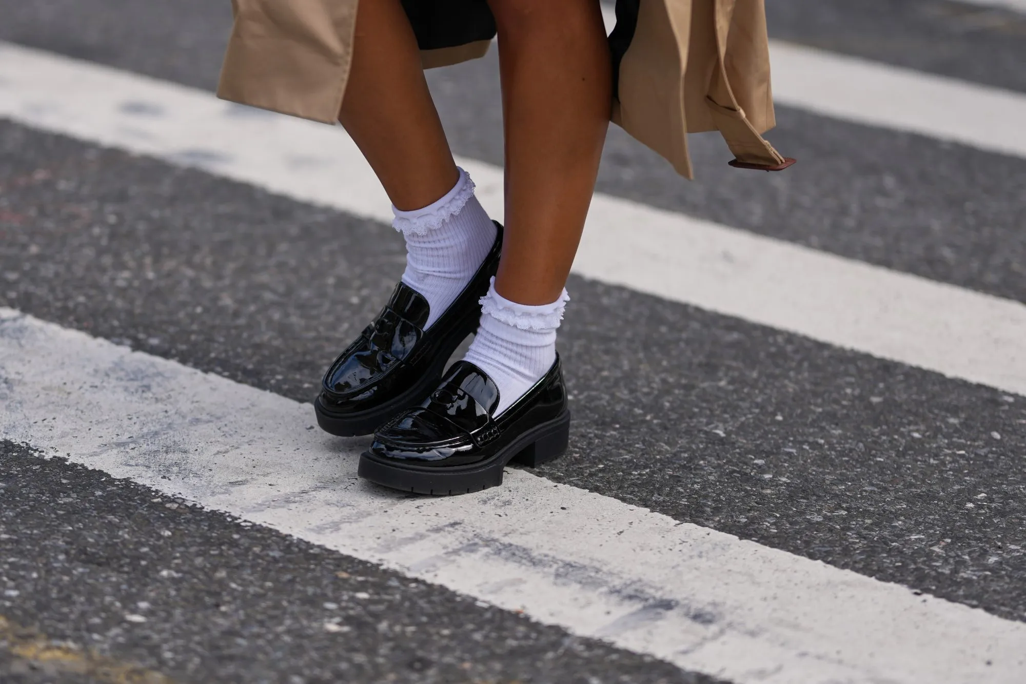 NEW YORK, NEW YORK - SEPTEMBER 15: A guest wears a beige trench coat, black patent varnished leather chunky lug-sole loafers shoes worn with white crew socks, outside Coach, during New York Fashion Week, on September 15, 2025 in New York, New York (Photo by Edward Berthelot/Getty Images)
