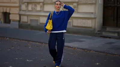 COLOGNE, GERMANY - SEPTEMBER 18: Evi Wave is seen wearing a cobalt blue knit sweater with an oversized fit and detailed neckline from American Vintage; a white t-shirt from Uniqlo; the Firebird, navy blue pleated track pants with white side stripes from Adidas; the Mexico 66, bright yellow lace-up sneakers with a black pattern on the side from Onitsuka Tiger; the Motocross Classic Work, large slouchy yellow leather bag with subtle details and seaming from Balenciaga; minimal metallic jewelry, featuring silver rings, layered necklaces and gold hoop earrings from Ariane Ernst; her brown hair is pulled back into a sleek low bun on September 18, 2025 in Cologne, Germany. (Photo by Moritz Scholz/Getty Images)