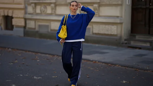 COLOGNE, GERMANY - SEPTEMBER 18: Evi Wave is seen wearing a cobalt blue knit sweater with an oversized fit and detailed neckline from American Vintage; a white t-shirt from Uniqlo; the Firebird, navy blue pleated track pants with white side stripes from Adidas; the Mexico 66, bright yellow lace-up sneakers with a black pattern on the side from Onitsuka Tiger; the Motocross Classic Work, large slouchy yellow leather bag with subtle details and seaming from Balenciaga; minimal metallic jewelry, featuring silver rings, layered necklaces and gold hoop earrings from Ariane Ernst; her brown hair is pulled back into a sleek low bun on September 18, 2025 in Cologne, Germany. (Photo by Moritz Scholz/Getty Images)