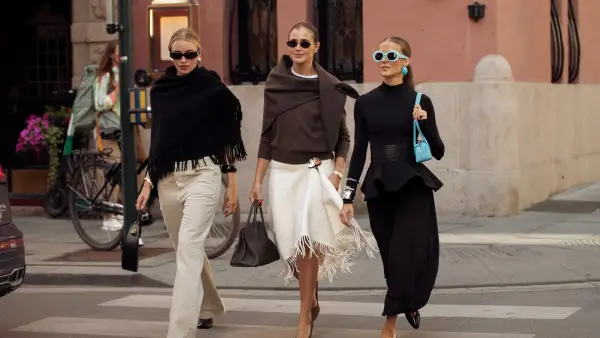 OSLO, NORWAY - AUGUST 26: (L-R) A guest wears beige pants, black sweater with tassels, Darja Barannik wears a brown sweater, beige skirt with tassels, and grey Hermes bag and Nina Sandbech wears a black balloon pants, black long sleeve top, blue bag, blue earrings and blue sunglasses outside the Christian Aks show during Oslo Fashion Week on August 26, 2025 in Oslo, Norway. (Photo by Raimonda Kulikauskiene/Getty Images)