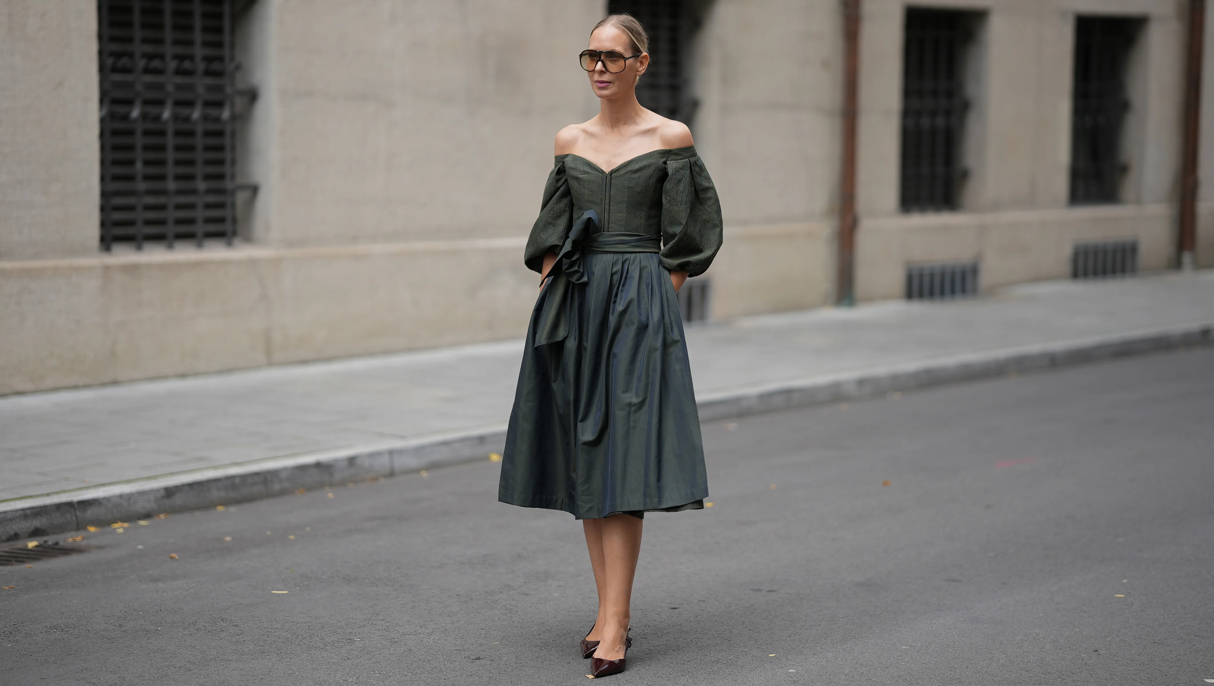 MUNICH, GERMANY - SEPTEMBER 1: Mirja Klein is seen wearing a off-the-shoulder dark green midi dress with voluminous, puffed sleeves and subtle floral texture throughout the bodice, the skirt is full and structured, cinched at the waist with a wide, matching sash tied in a bow from Cocovero; pointed-toe heels in a burgundy patent leather from Mango; oversized brown-tinted aviator sunglasses with a thin frame from Tom Ford; her blonde hair is pulled back in a sleek low bun on September 1, 2025 in Munich, Germany. (Photo by Moritz Scholz/Getty Images)