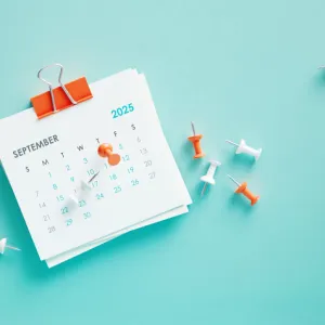 September 2025 calendar and thumbtacks on blue background. Horizontal composition. Reminder concept.