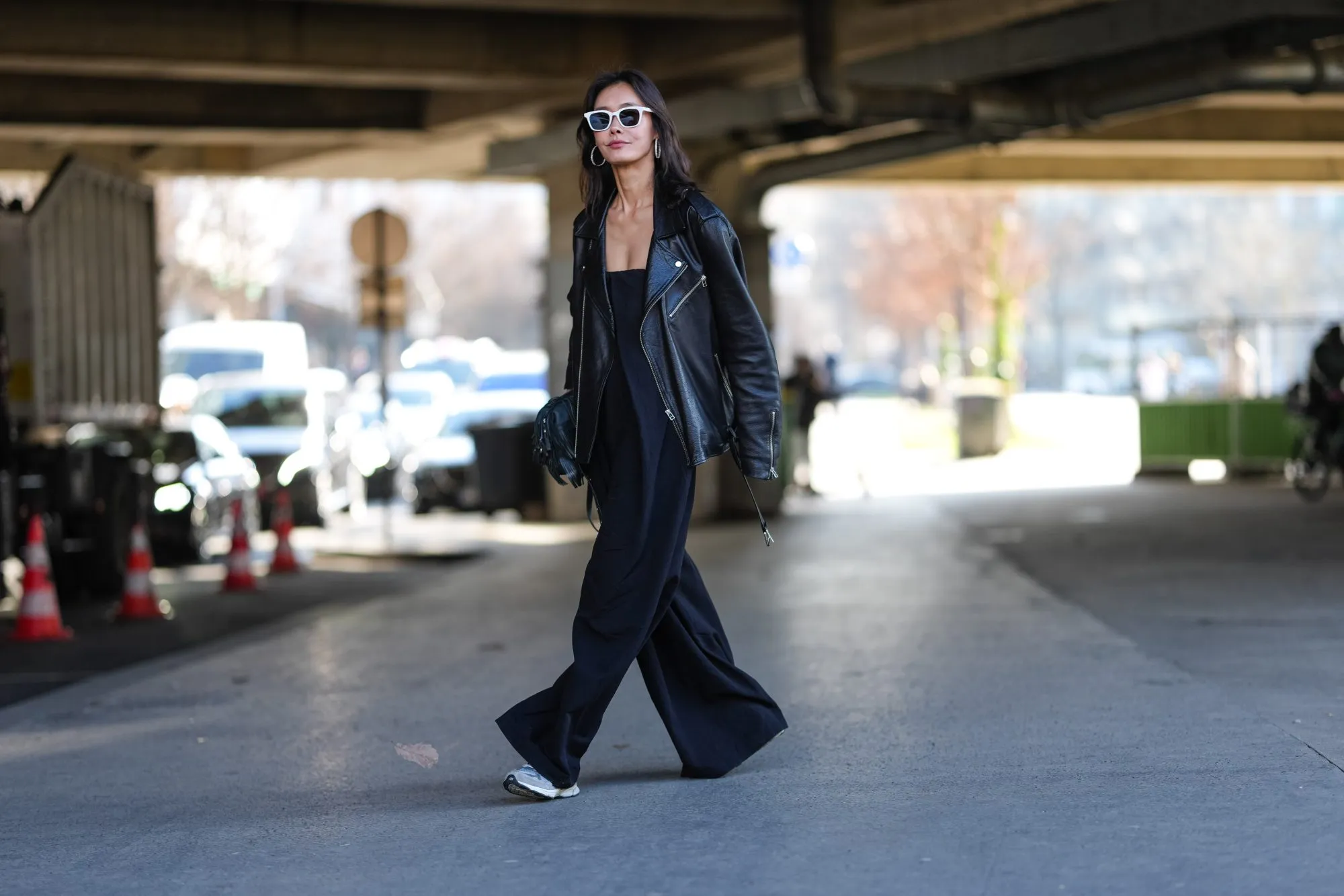 PARIS, FRANCE - MARCH 05: A guest wears white sunglasses, silver hoop earrings, shiny black oversized leather jacket, shiny black leather bag, black sleeveless flowy romper, light gray sneaker shoes, outside Stella McCartney, during the Paris Fashion week Women's Fall/Winter 2025-2026 on March 5, 2025 in Paris, France. (Photo by Edward Berthelot/Getty Images)