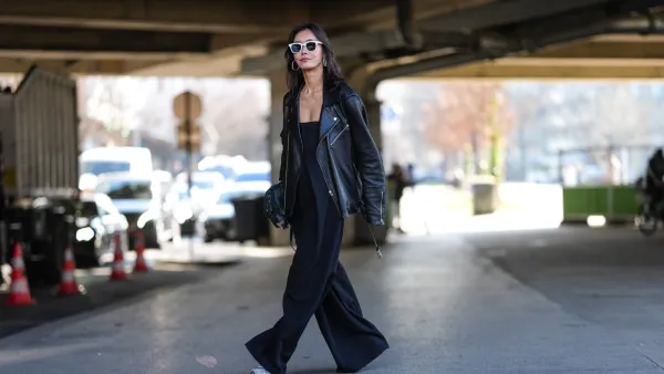 PARIS, FRANCE - MARCH 05: A guest wears white sunglasses, silver hoop earrings, shiny black oversized leather jacket, shiny black leather bag, black sleeveless flowy romper, light gray sneaker shoes, outside Stella McCartney, during the Paris Fashion week Women's Fall/Winter 2025-2026 on March 5, 2025 in Paris, France. (Photo by Edward Berthelot/Getty Images)