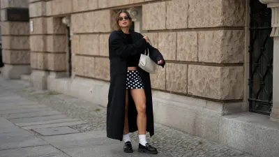 BERLIN, GERMANY - SEPTEMBER 1: Sonia Lyson is seen wearing a long, oversized black coat with broad shoulders and a straight cut, worn open from 032C; a simple black crop top leaving the midriff slightly visible from Zara; a short, fitted black-and-white polka dot mini skirt from Attega; black chunky loafers paired with white socks from LeGer by Lena Gercke; a medium sized white leather handbag with shoulder straps from Demmilie London; small, sleek black sunglasses that are oval shaped from Vela Eyewear; her brown hair is pulled back into a slightly messy low bun on September 1, 2025 in Berlin, Germany. (Photo by Moritz Scholz/Getty Images)