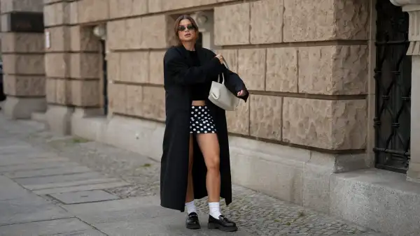 BERLIN, GERMANY - SEPTEMBER 1: Sonia Lyson is seen wearing a long, oversized black coat with broad shoulders and a straight cut, worn open from 032C; a simple black crop top leaving the midriff slightly visible from Zara; a short, fitted black-and-white polka dot mini skirt from Attega; black chunky loafers paired with white socks from LeGer by Lena Gercke; a medium sized white leather handbag with shoulder straps from Demmilie London; small, sleek black sunglasses that are oval shaped from Vela Eyewear; her brown hair is pulled back into a slightly messy low bun on September 1, 2025 in Berlin, Germany. (Photo by Moritz Scholz/Getty Images)