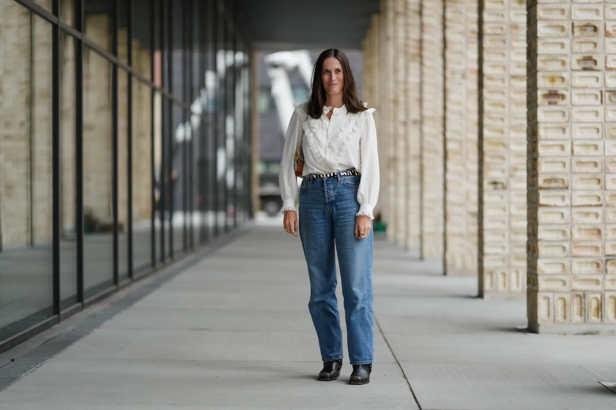 COPENHAGEN, DENMARK - AUGUST 07: Astrid Boutrot wears a white blouse featuring ruffled detailing along the front and cuffs, paired with high-waisted blue denim jeans. The ensemble is accessorized with a black and white patterned belt. Black ankle boots complete the outfit. Hair is styled straight and loose, outside Birrot, during Copenhagen Fashion Week, on August 07, 2025 in Copenhagen, Denmark (Photo by Edward Berthelot/Getty Images)