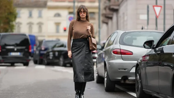 MILAN, ITALY - SEPTEMBER 26: Alison Toby wears wavy medium-length brown hair with a center part, tortoiseshell oval sunglasses, a gold bracelet and a gold ring, a brown leather shoulder bag, a brown long-sleeve knit turtleneck sweater tucked into a black leather midi skirt with a wrap seam and high waist, black leather knee-high boots shoes with a low block heel, outside Tod's, during Milan Fashion Week - Womenswear Spring/Summer 2026, on September 26, 2025 in Milan, Italy (Photo by Edward Berthelot/Getty Images)