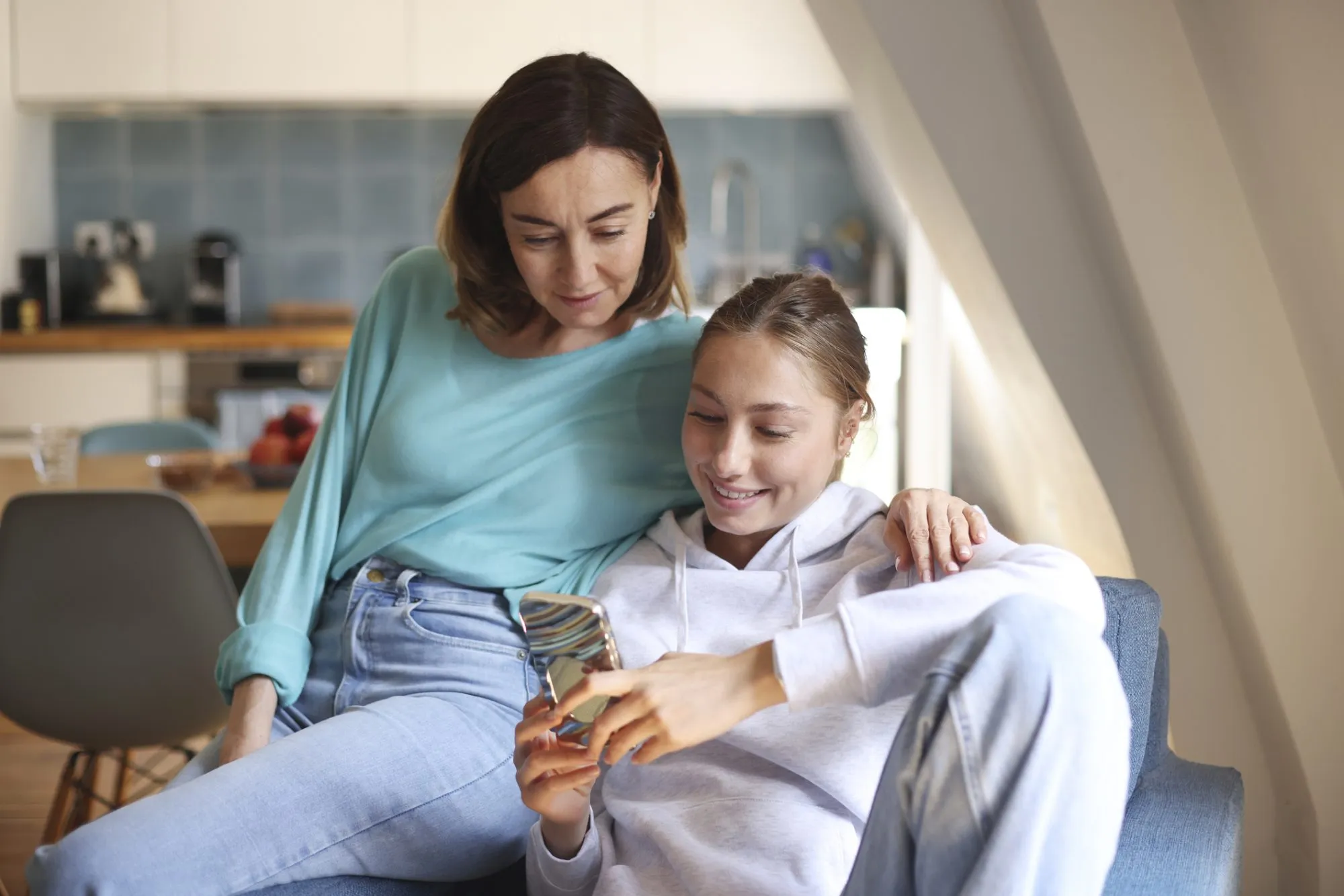 A mom and daughter spending time together, looking at a phone, in the living room. Photo by Catherine Delahaye/Getty Images