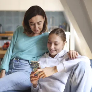 A mom and daughter spending time together, looking at a phone, in the living room. Photo by Catherine Delahaye/Getty Images