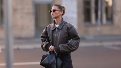 BERLIN, GERMANY - OCTOBER 12: Sophia Geiss is seen wearing oval rimless black sunglasses from Vehla Eyewear, two different-sized gold hoop earrings, a silver nose ring, a cropped dark brown leather jacket with wide sleeves and ribbed cotton cuffs from Meotine, a white top underneath, wide-legged dark vintage jeans with orange decorative seams, a silver ring, and a black leather bag with round handles from COS on October 12, 2024 in Berlin, Germany. (Photo by Jeremy Moeller/Getty Images)