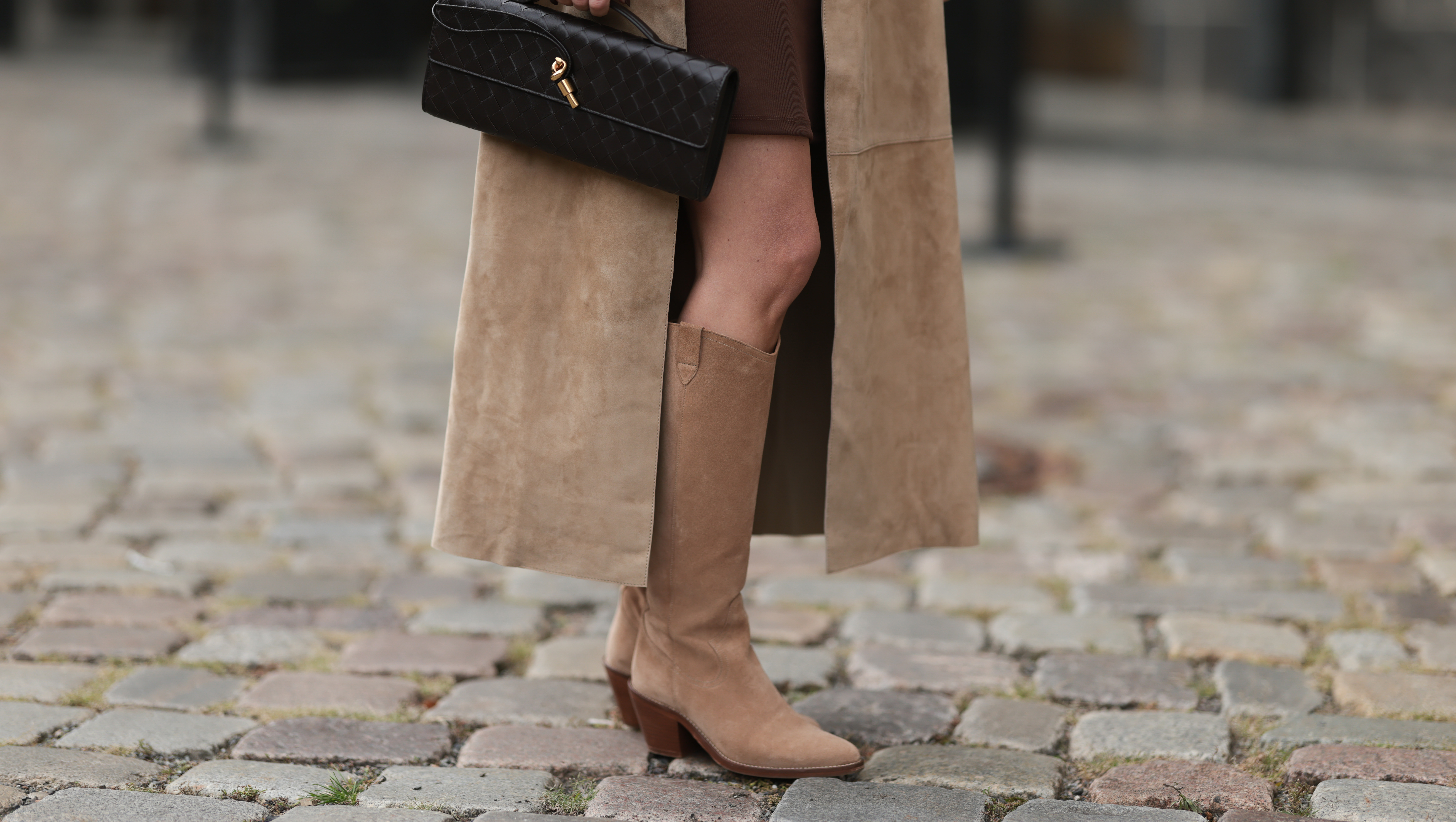 BERLIN, GERMANY - SEPTEMBER 17: Yana Pries seen wearing a long suede leather trench coat from NOUR HAMMOUR in a warm beige tone, underneath she wears Even&Odd fitted chocolate-brown mini dress, Bottega Veneta Andiamo clutch, a structured black leather bag with a gold knot detail and Bobbies knee-high Bobbies suede leather boots in a soft beige tone, on September 17, 2025 in Berlin, Germany. (Photo by Jeremy Moeller/Getty Images)