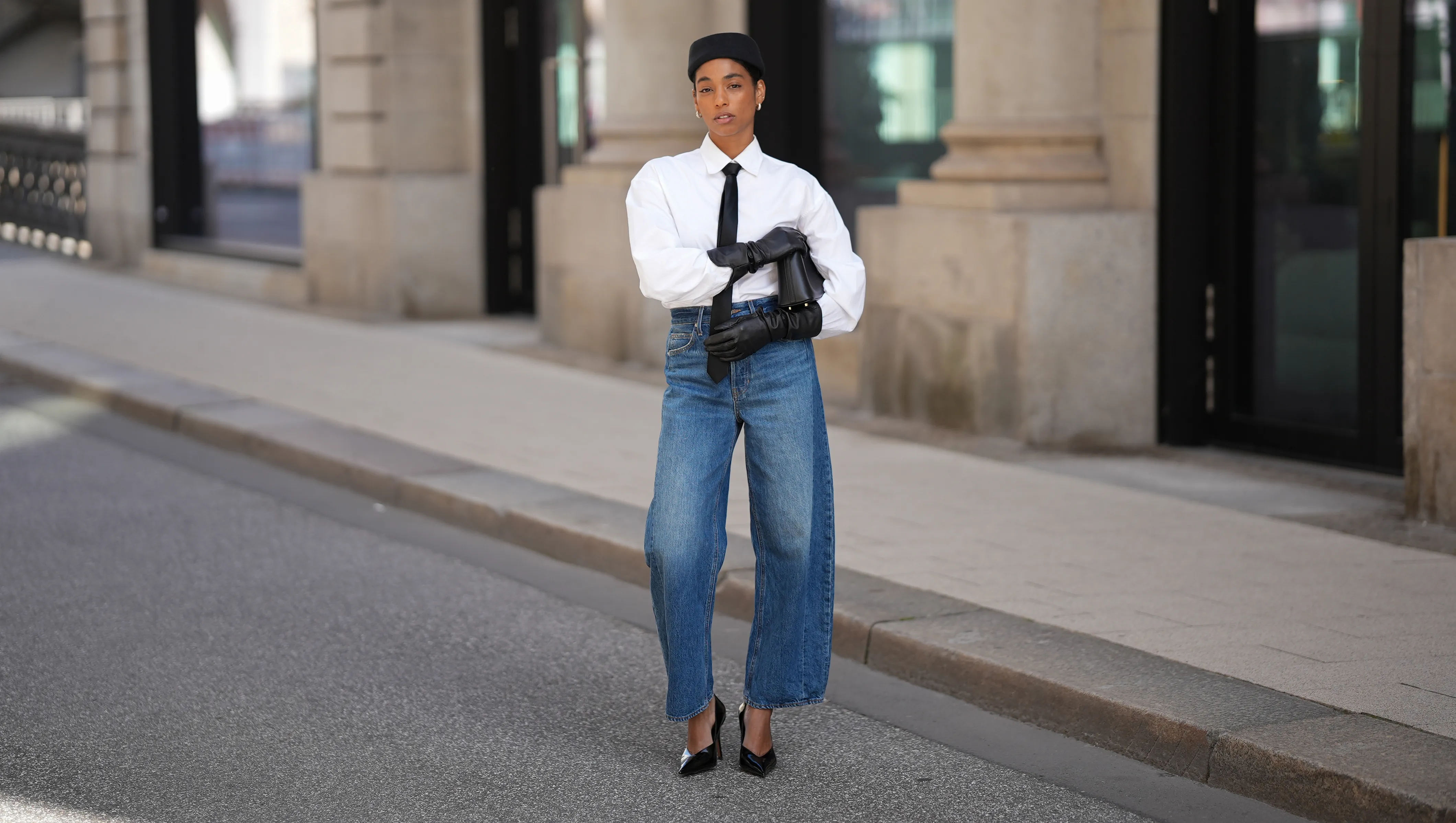 HAMBURG, GERMANY - AUGUST 17: Cherifa Akili is seen wearing a long-sleeved white button-down blouse from Closed, tucked into the jeans; a slim black necktie from Drykorn; high-waisted, wide-leg blue jeans in a mid-wash denim from Veronica Beard; black leather gloves on both hands covering the wrists and forearms from Zara; a black leather handbag with a golden top handle, carried in one hand from Elle Me; A small, fitted black pillbox-style hat; her hair is tucked into a slight bun; shiny-black pointed-toe stiletto pumps from 10TH FLOOR; narrow sunglasses with slightly angular edges and dark tinted lenses from Ysl on August 17, 2025 in Hamburg, Germany. (Photo by Moritz Scholz/Getty Images)