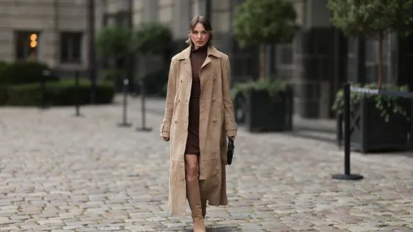 BERLIN, GERMANY - SEPTEMBER 17: Yana Pries seen wearing a long suede leather trench coat from NOUR HAMMOUR in a warm beige tone. The coat features double-breasted buttons, a structured collar, and belted cuffs, creating a luxurious yet timeless silhouette. Her hair is cut into a sleek bob, light brown with subtle highlights, styled with a middle part and softly curved ends that frame her face. Underneath she wears Even&Odd fitted chocolate-brown mini dress, with a high neckline, Bottega Veneta Andiamo clutch, a structured black leather bag with a gold knot detail on the strap and Bobbies knee-high Bobbies suede leather boots in a soft beige tone, on September 17, 2025 in Berlin, Germany. (Photo by Jeremy Moeller/Getty Images)