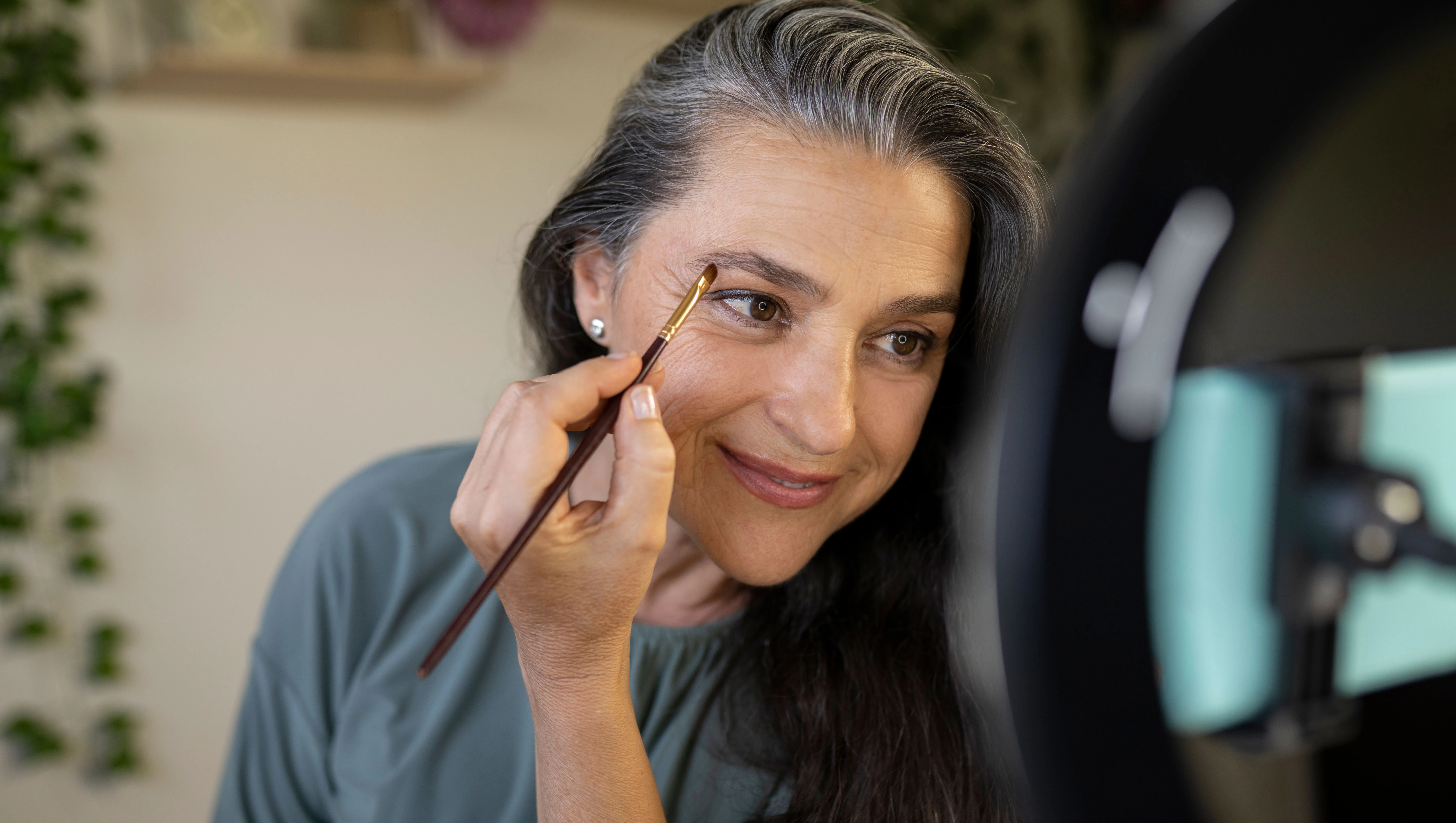 Smiling female vlogger brushing eyebrows during tutorial at home - stock photo