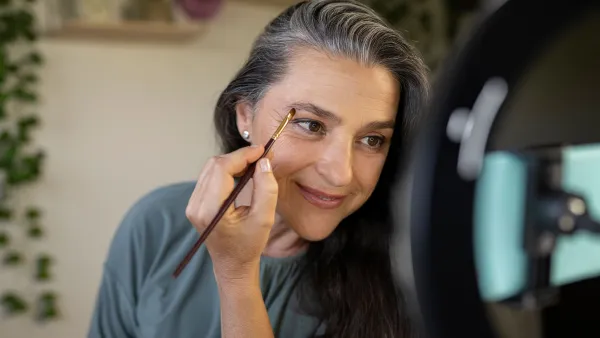 Smiling female vlogger brushing eyebrows during tutorial at home - stock photo