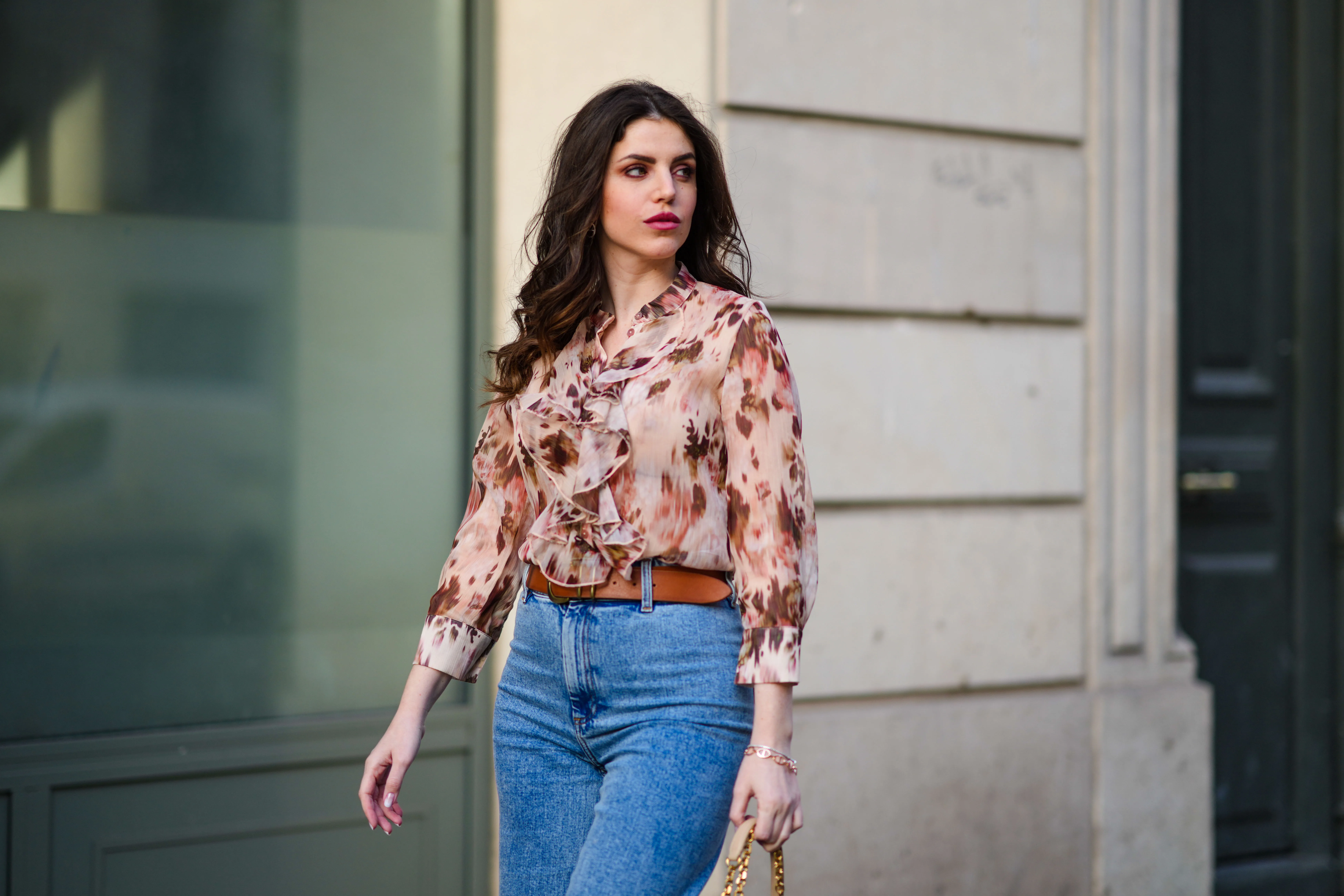 Sara Carnicella @lafillerebelle wears earrings from APM Monaco, a pink and purple floral print flowing shirt from Liu Jo, a brown leather belt from Mango, blue denim flared jeans from & Other Stories, on March 28, 2021 in Paris, France.