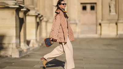 Alba Garavito Torre wears pearls earrings, black wayfarer sunglasses from Ray Ban, a beige quilted oversized jacket from Munthe, a white and yellow silk scarf tie with classic knot from Lollys Laundry, a brown / beige braided wool pullover from Polo Ralph Lauren, a brown shiny leather belt, high waist beige palazzo pants from Bimba y Lola, a blue denim monogram and brown shiny leather Jackie 1961 Mini bag handbag from Gucci, yellow mustard suede block heels ankle boots, gold bracelets, gold rings, during a street style fashion photo session, on November 12, 2021 in Paris, France.