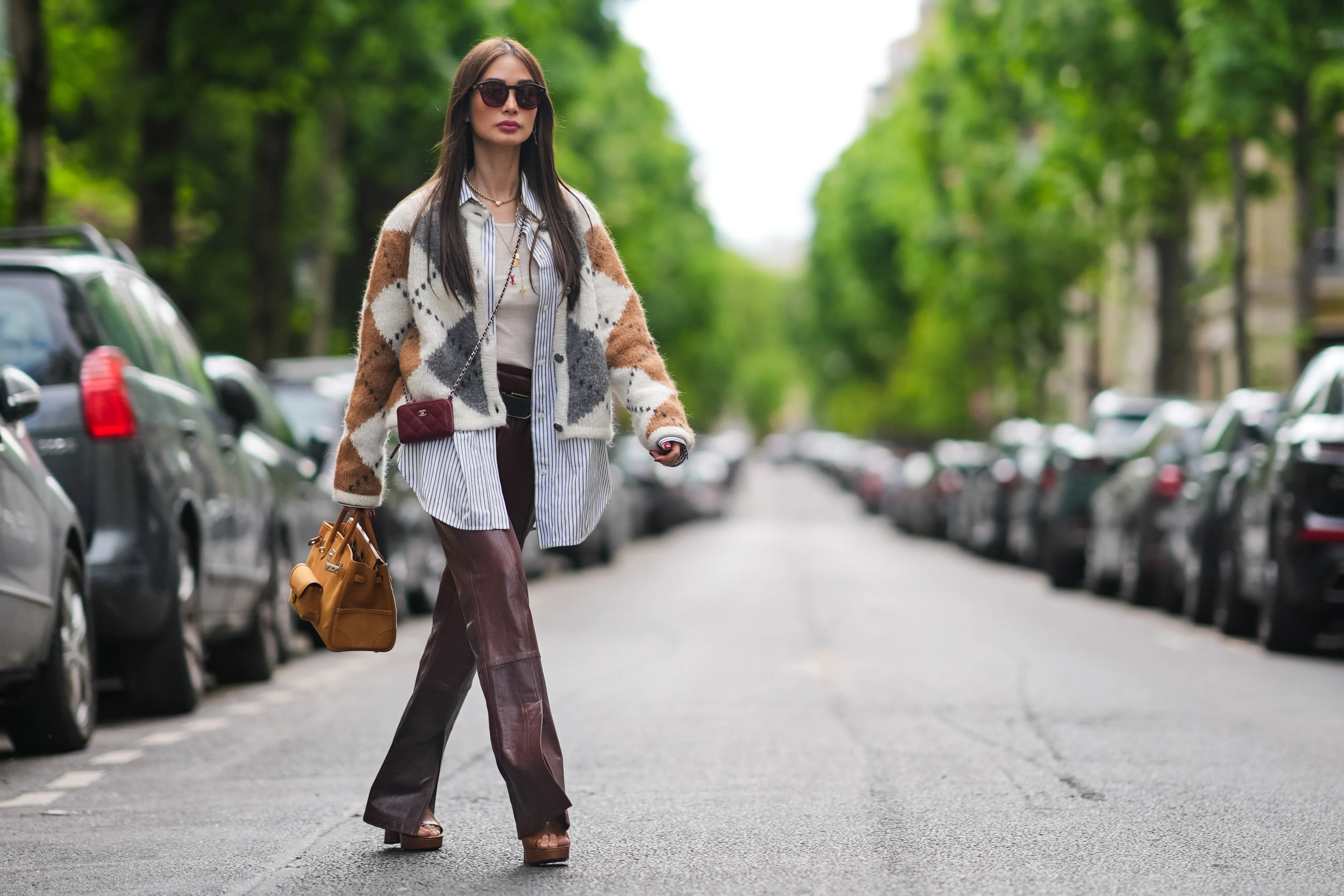 PARIS, FRANCE - APRIL 27: Heart Evangelista wears sunglasses, a golden necklace, a gray brown and white wool cardigan with checked patterns, a white t-shirt from Saint-Laurent YSL, a belt, burgundy slit leather pants , a burgundy leather mini quilted Chanel bag, an orange / brown large Hermes bag, brown shoes, during a street style fashion photo session, on April 27, 2024 in Paris, France. (Photo by Edward Berthelot/Getty Images)