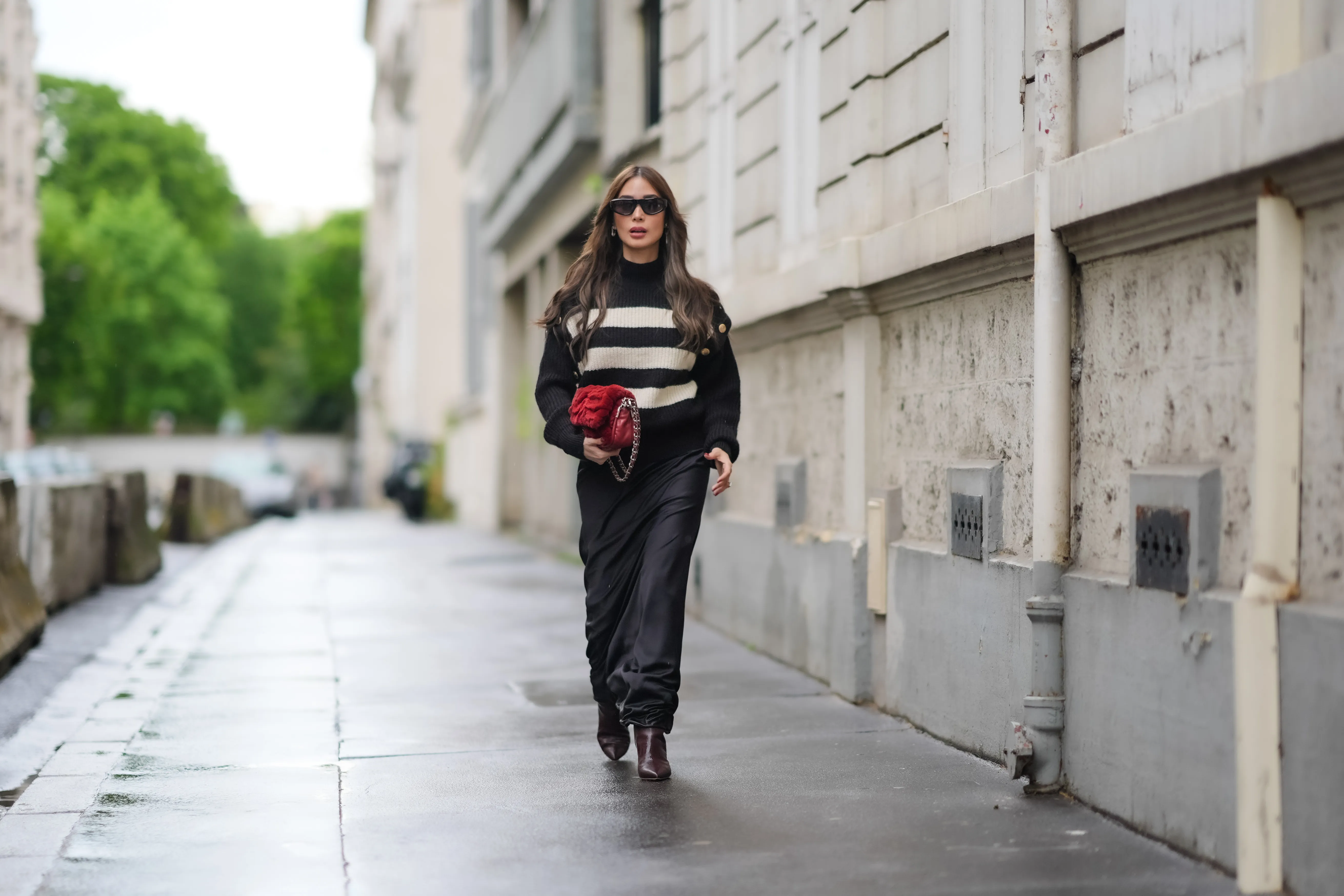 PARIS, FRANCE - APRIL 27: Heart Evangelista wears sunglasses, a black and white striped ribbed turtleneck pullover with golden buttons on the shoulders, a red fluffy Chanel bag, a black satin silky lustrous flowing skirt , brown pointed boots, during a street style fashion photo session, on April 27, 2024 in Paris, France. (Photo by Edward Berthelot/Getty Images)