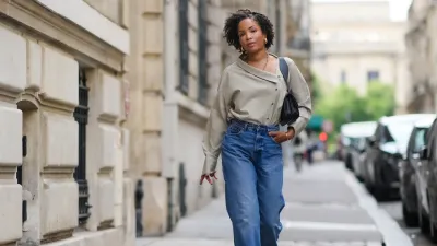 PARIS, FRANCE - MAY 20: Ellie Delphine wears golden earrings, a necklace from Missoma a beige oversized off-shoulder top / shirt from The Frankie Shop, blue wide-leg denim pants / jeans from H&M, a black leather bag from Neous, T sandals / heels shoes from Neous, during a street style fashion photo session, on May 20, 2024 in Paris, France. (Photo by Edward Berthelot/Getty Images)