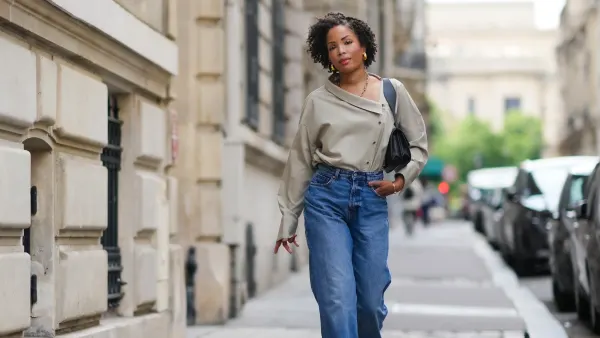 PARIS, FRANCE - MAY 20: Ellie Delphine wears golden earrings, a necklace from Missoma a beige oversized off-shoulder top / shirt from The Frankie Shop, blue wide-leg denim pants / jeans from H&M, a black leather bag from Neous, T sandals / heels shoes from Neous, during a street style fashion photo session, on May 20, 2024 in Paris, France. (Photo by Edward Berthelot/Getty Images)