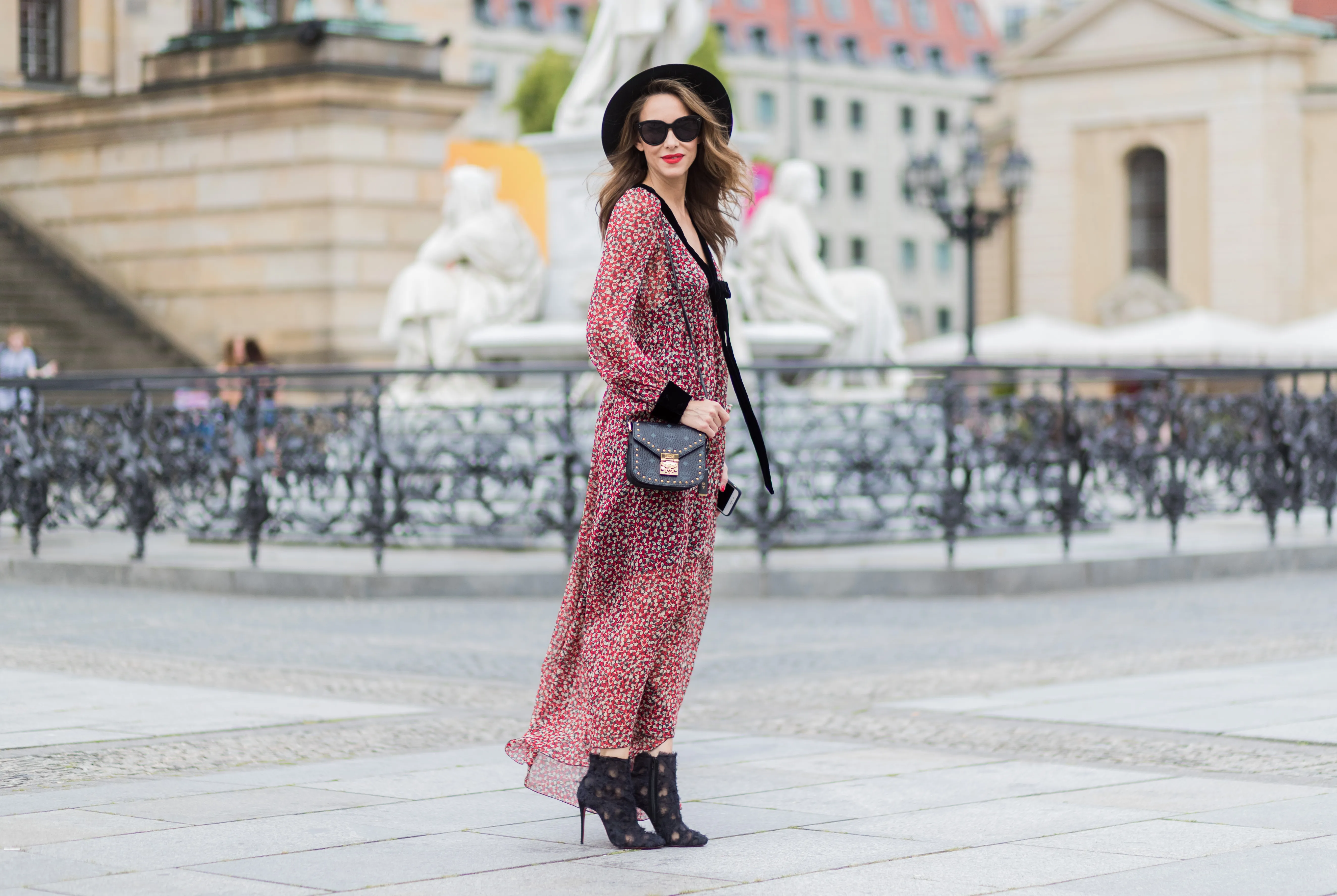 Alexandra Lapp wearing Boho Style, a red and cream floral print maxi dress from Philosophy di Lorenzo Serafini in sheer silk chiffon and bold black trims with a ribbon tie, Toubootfrou ankle boots with rete, organze and suede in black from Christian Louboutin, Celine Audrey sunglasses in black, Maison Maison Michel hat Virginie fedora, MCM Patricia Shoulder Bag in a vintage shape during the Mercedes-Benz Fashion Week Berlin Spring/Summer 2018 on July 7, 2017 in Berlin, Germany.