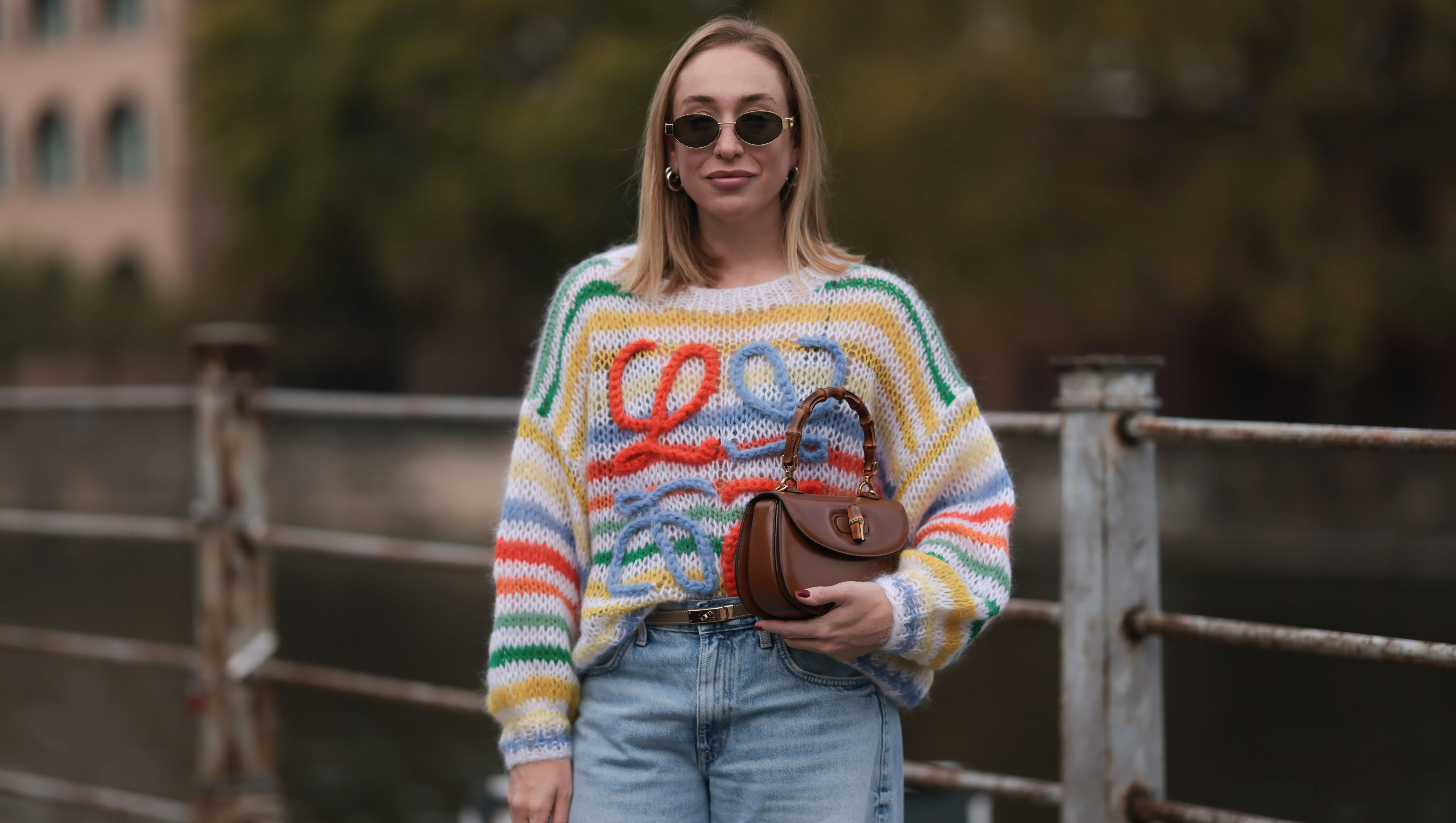BERLIN, GERMANY - OCTOBER 25: Sonia Lyson seen wearing Celine gold Triomphe oval shaped sunglasses, silver earrings, Loewe colorful striped wool knit sweater, Herm&egrave;s Kelly brown leather belt, Zara light blue wide leg denim / jeans pants, Gucci brown leather Bamboo bag, on October 25, 2023 in Berlin, Germany. (Photo by Jeremy Moeller/Getty Images)