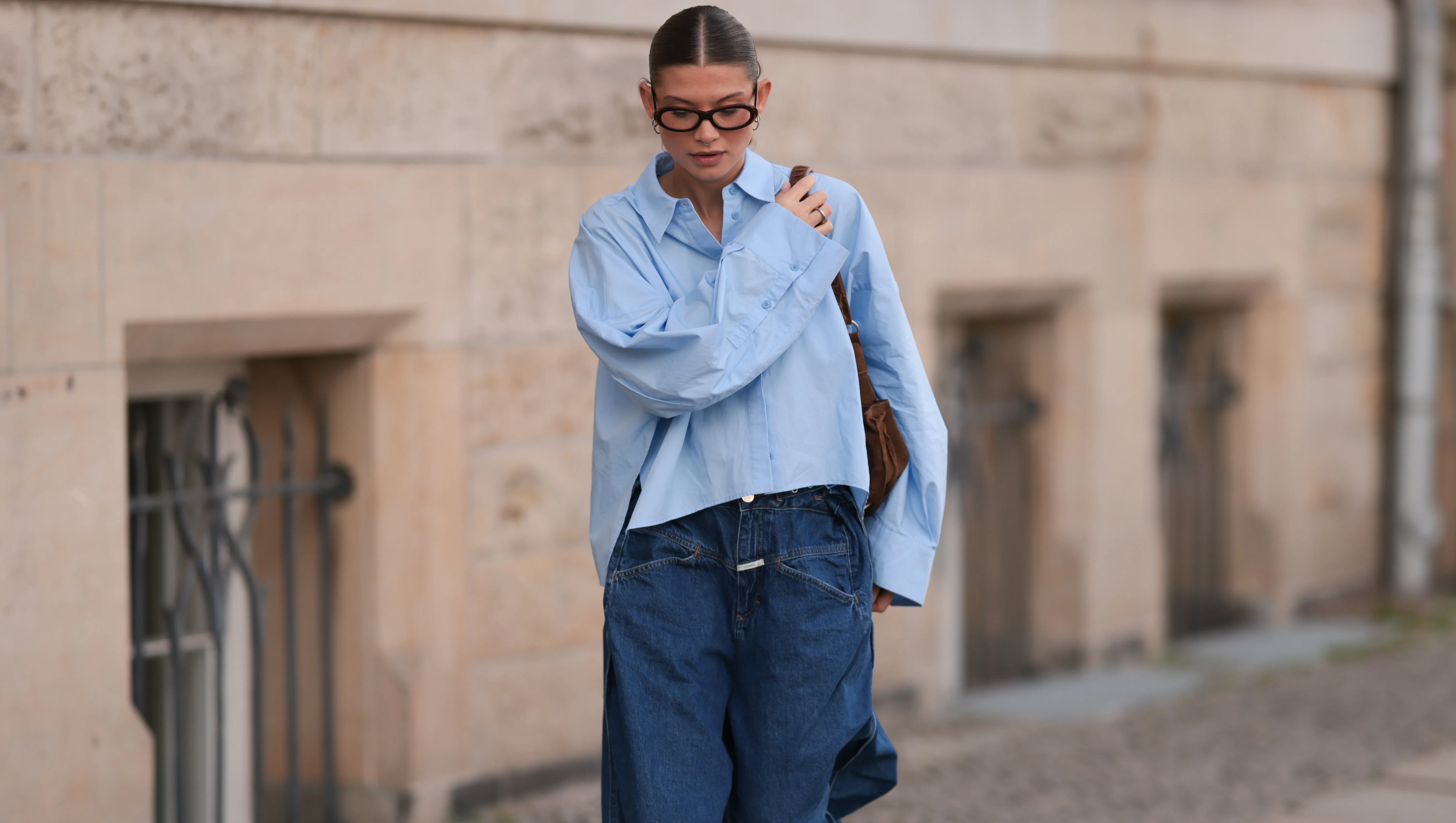 BERLIN, GERMANY - APRIL 22: Sophia Geiss is seen wearing two different-sized silver hoop earrings, oval brown glasses from Corlin, a silver nose ring, an oversized light blue shirt from Drykorn, wide-leg jeans with orange decorative seams from Closed, a silver ring, a brown vintage suede bag, and dark brown leather boots with chunky soles from Miista on April 22, 2025 in Berlin, Germany. (Photo by Jeremy Moeller/Getty Images)