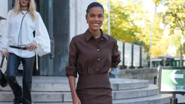 PARIS, FRANCE - OCTOBER 07: Tina Kunakey wears hair pulled back into a sleek low bun, dark brown hair, small polished gold hoop earrings, a brown long-sleeve button-front shirt in a lightweight woven fabric with a pointed collar and gold buttons / rolled sleeves, a matching brown high-waisted fitted midi skirt with side slits, brown leather strappy sandals shoes with thin stiletto heels and a single ankle strap, outside AJE, during Paris Fashion Week - Womenswear Spring Summer 2026, on October 07, 2025 in Paris, France (Photo by Edward Berthelot/Getty Images)