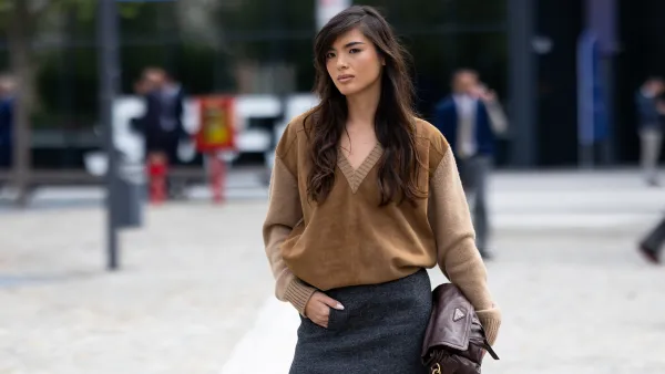 MILAN, ITALY - SEPTEMBER 25: A guest wears a dark brown leather Prada bag, a grey midi skirt and a wool and suede v-neck sweater outside Prada show during the Milan Fashion Week Womenswear Spring/Summer 2026 on September 25, 2025 in Milan, Italy. (Photo by Valentina Frugiuele/Getty Images)