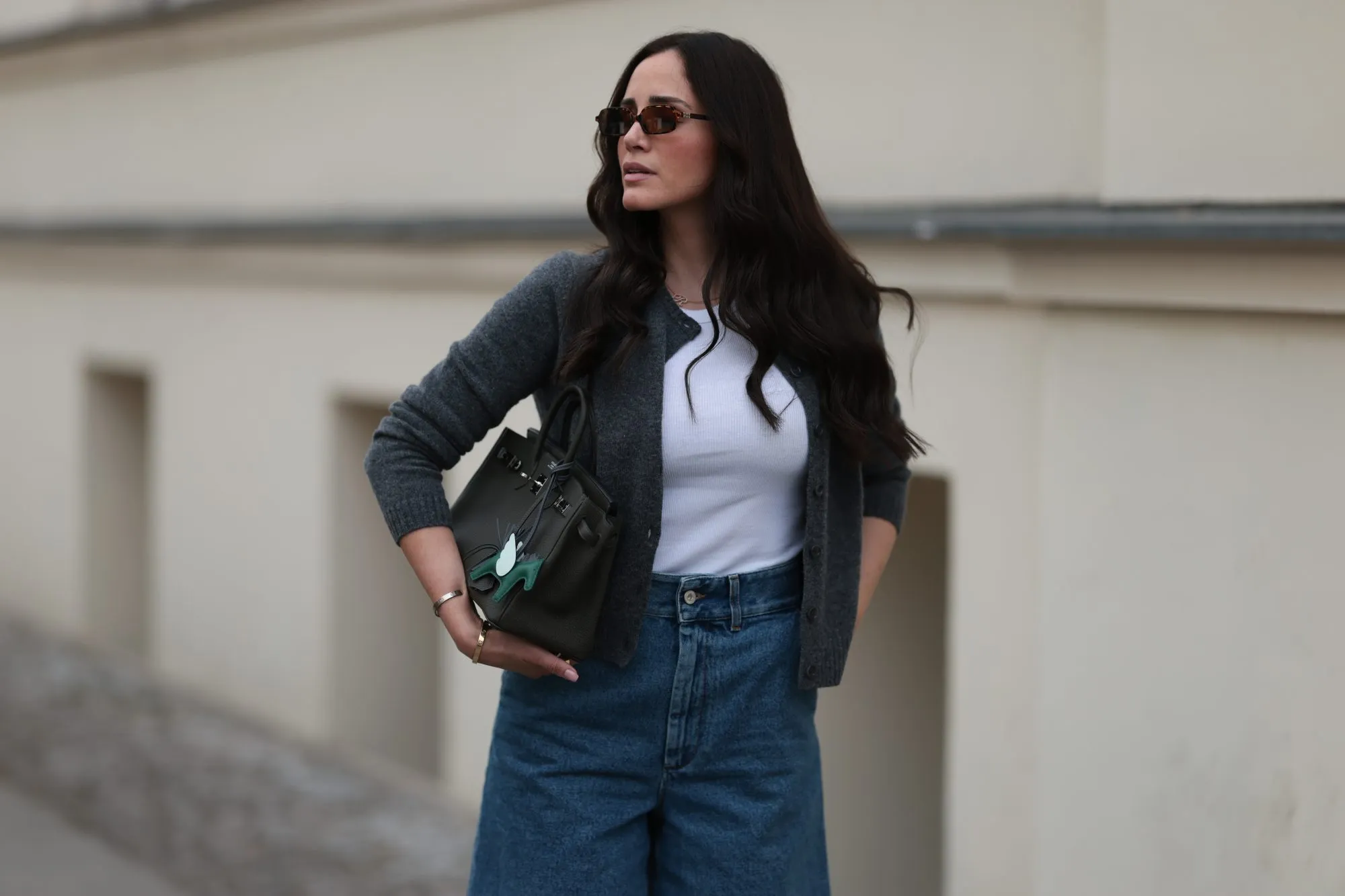 BERLIN, GERMANY - JUNE 27: Raffaela Taschlizki is seen wearing rectangular Havana-framed sunglasses with brown lenses and thin temples from Miu Miu; a gold necklace with a diamond-studded letter pendant; an unbuttoned grey wool cardigan, paired with a white tank top underneath, both from Zara; denim shorts with white logo embroidery at the front from Loewe; a rectangular black leather &ldquo;Birkin&rdquo; bag with a horse-shaped &ldquo;Rodeo&rdquo; bag charm, both from Herm&egrave;s; and two &ldquo;Love&rdquo; bracelets in yellow gold and white gold from Cartier on June 27, 2025 in Berlin, Germany. (Photo by Jeremy Moeller/Getty Images)