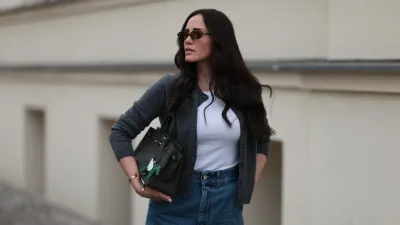 BERLIN, GERMANY - JUNE 27: Raffaela Taschlizki is seen wearing rectangular Havana-framed sunglasses with brown lenses and thin temples from Miu Miu; a gold necklace with a diamond-studded letter pendant; an unbuttoned grey wool cardigan, paired with a white tank top underneath, both from Zara; denim shorts with white logo embroidery at the front from Loewe; a rectangular black leather “Birkin” bag with a horse-shaped “Rodeo” bag charm, both from Hermès; and two “Love” bracelets in yellow gold and white gold from Cartier on June 27, 2025 in Berlin, Germany. (Photo by Jeremy Moeller/Getty Images)