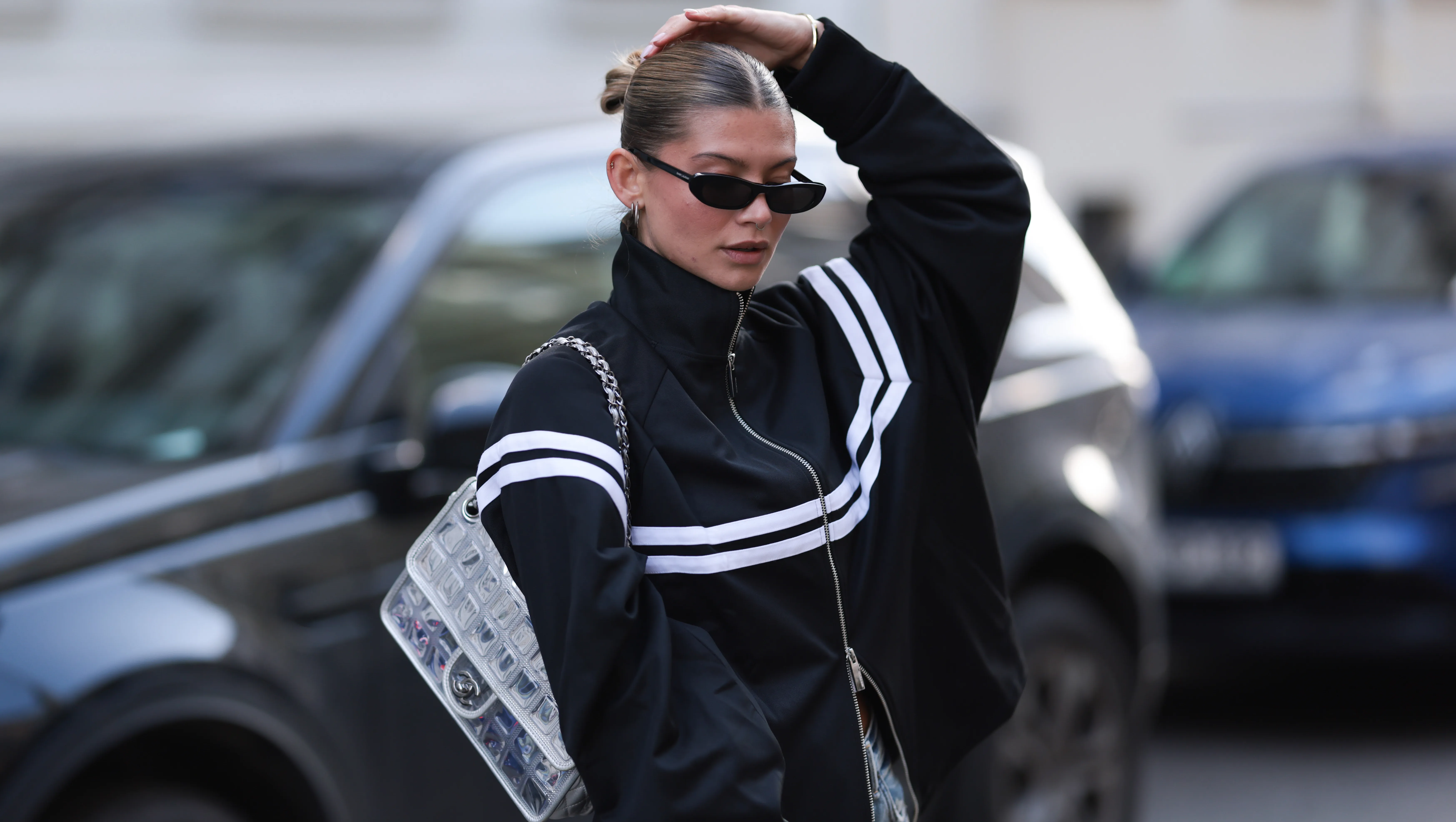 BERLIN, GERMANY - APRIL 08: Sophia Geiss seen wearing Yves Saint Laurent bold, rectangular black sunglasses, minimal hoop earrings, Black Palms sporty black zip-up with high collar and oversized fit tracking jacket featuring bold white horizontal stripes across the chest and sleeves, Acne Studios wide-leg dirty jeans that are intentionally distressed and splattered with white paint, Chanel silver metallic flap bag / standout silver quilted handbag with a chunky chain strap, on April 08, 2025 in Berlin, Germany. (Photo by Jeremy Moeller/Getty Images)