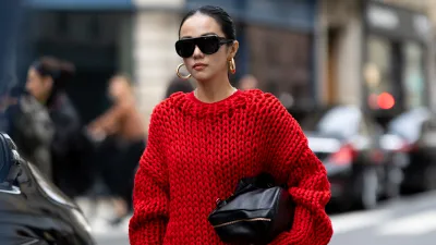 PARIS, FRANCE - OCTOBER 06: Yoyo Cao wears an oversized chunky red knit sweater with a matching red mini skirt, black knee-high heeled boots, black oversized sunglasses, and gold hoop earrings, carrying a black clutch outside Sacai show during the Womenswear Spring Summer 2026 as part of Paris Fashion Week on October 06, 2025 in Paris, France. (Photo by Valentina Frugiuele/Getty Images)