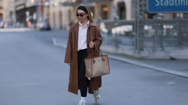 BERLIN, GERMANY - APRIL 09: Sonia Lyson seen wearing black cotton headband, Corlin Eyewear slim oval-shaped dark brown sunglasses, Worst Behavior white cotton polo sweater giving the look a sporty, laid-back vibe, Herskind long, cognac brown leather trench coat, Lululemon simple black comfortable and athleisure-inspired leggings, Gianni Chiarini large beige tote bag with brown leather trim and monogrammed initials, Nike white cotton crew socks and New Balance chunky cream white sneakers, on April 09, 2025 in Berlin, Germany. (Photo by Jeremy Moeller/Getty Images)