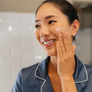 Japanese woman looking her skin in the mirror, applying facial creme and preparing her self before going to work in the bathroom