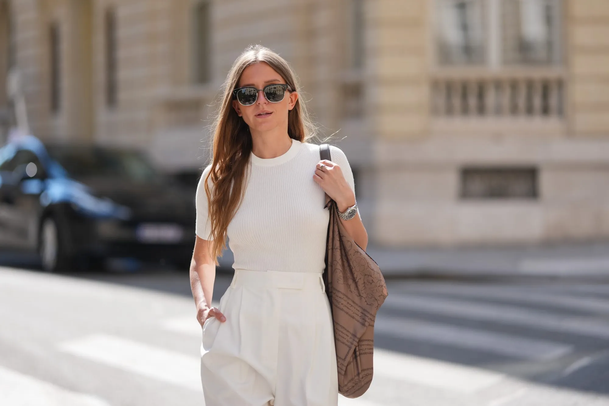 PARIS, FRANCE - APRIL 28: Diane Batoukina wears black sunglasses, long straight brown hair with a center part, a fitted ribbed white short-sleeve T-shirt tucked into high-waisted pleated off-white pants. A brown printed shoulder bag with script and pattern motifs is worn over one shoulder, accessorized with a silver watch. Mid shot, during a street style fashion photo session, on April 28, 2025 in Paris, France. (Photo by Edward Berthelot/Getty Images)