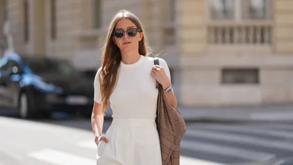 PARIS, FRANCE - APRIL 28: Diane Batoukina wears black sunglasses, long straight brown hair with a center part, a fitted ribbed white short-sleeve T-shirt tucked into high-waisted pleated off-white pants. A brown printed shoulder bag with script and pattern motifs is worn over one shoulder, accessorized with a silver watch. Mid shot, during a street style fashion photo session, on April 28, 2025 in Paris, France. (Photo by Edward Berthelot/Getty Images)