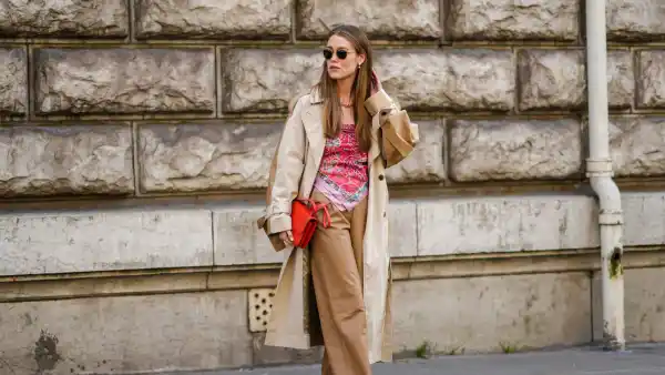 PARIS, FRANCE - MARCH 05: Annabel Rosendahl wears sunglasses, pearls pendant earrings, a gold large chain necklace, a beige and brown long oversized coat, a red shiny leather Constance shoulder bag from Hermes, a red / pink / green / black print pattern silk scarf as a shoulder-off t-shirt, brown shiny leather wide legs pants, black shiny leather pointed pumps heels shoes, outside Hermes , during Paris Fashion Week - Womenswear F/W 2022-2023, on March 05, 2022 in Paris, France. (Photo by Edward Berthelot/Getty Images)