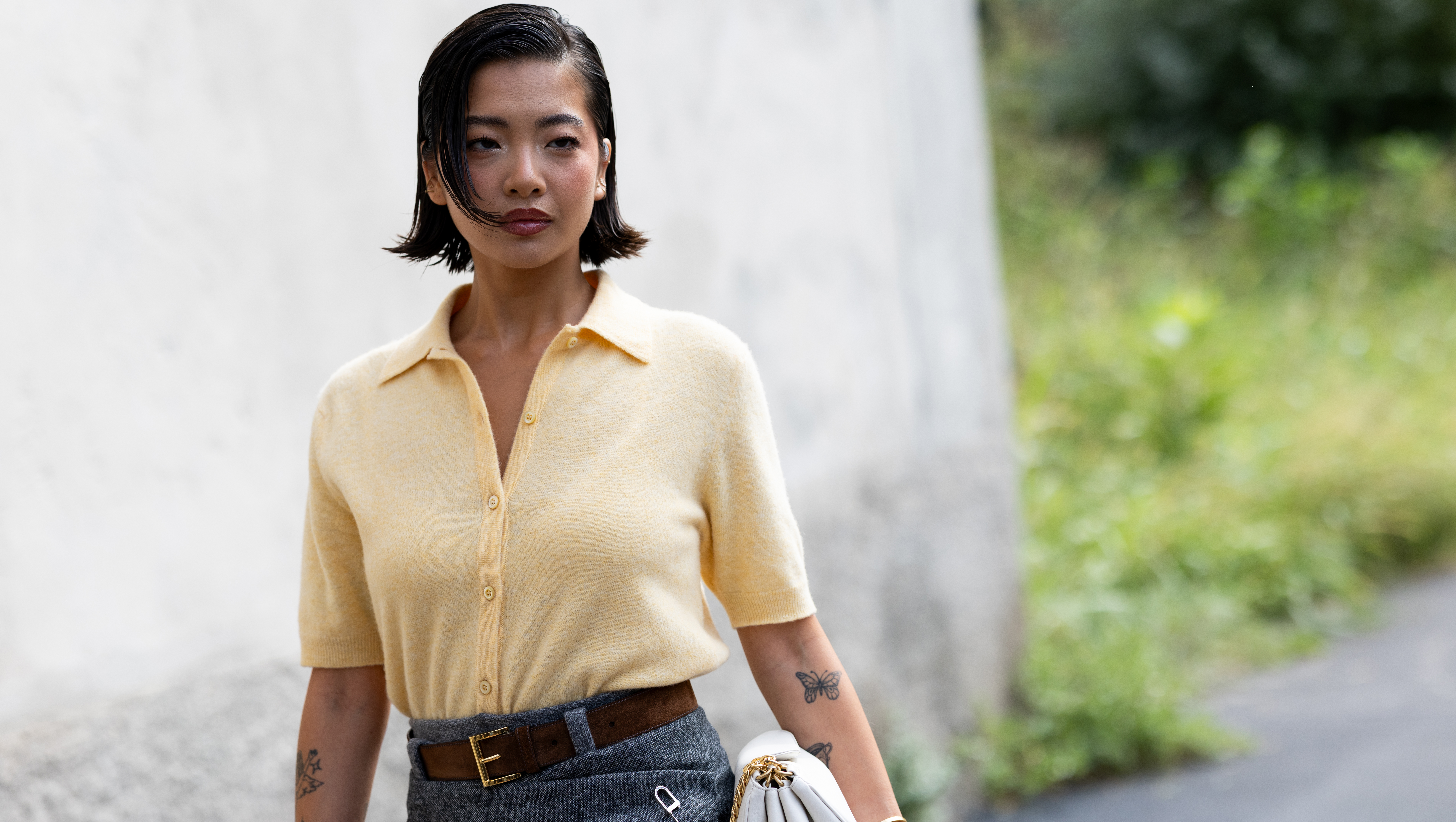 MILAN, ITALY - SEPTEMBER 25: A guest wears a polo styled light yellow short sleeved cardigan, a brown leather belt, a white leather bag and a grey mini skirt outside Prada show during the Milan Fashion Week Womenswear Spring/Summer 2026 on September 25, 2025 in Milan, Italy. (Photo by Valentina Frugiuele/Getty Images)