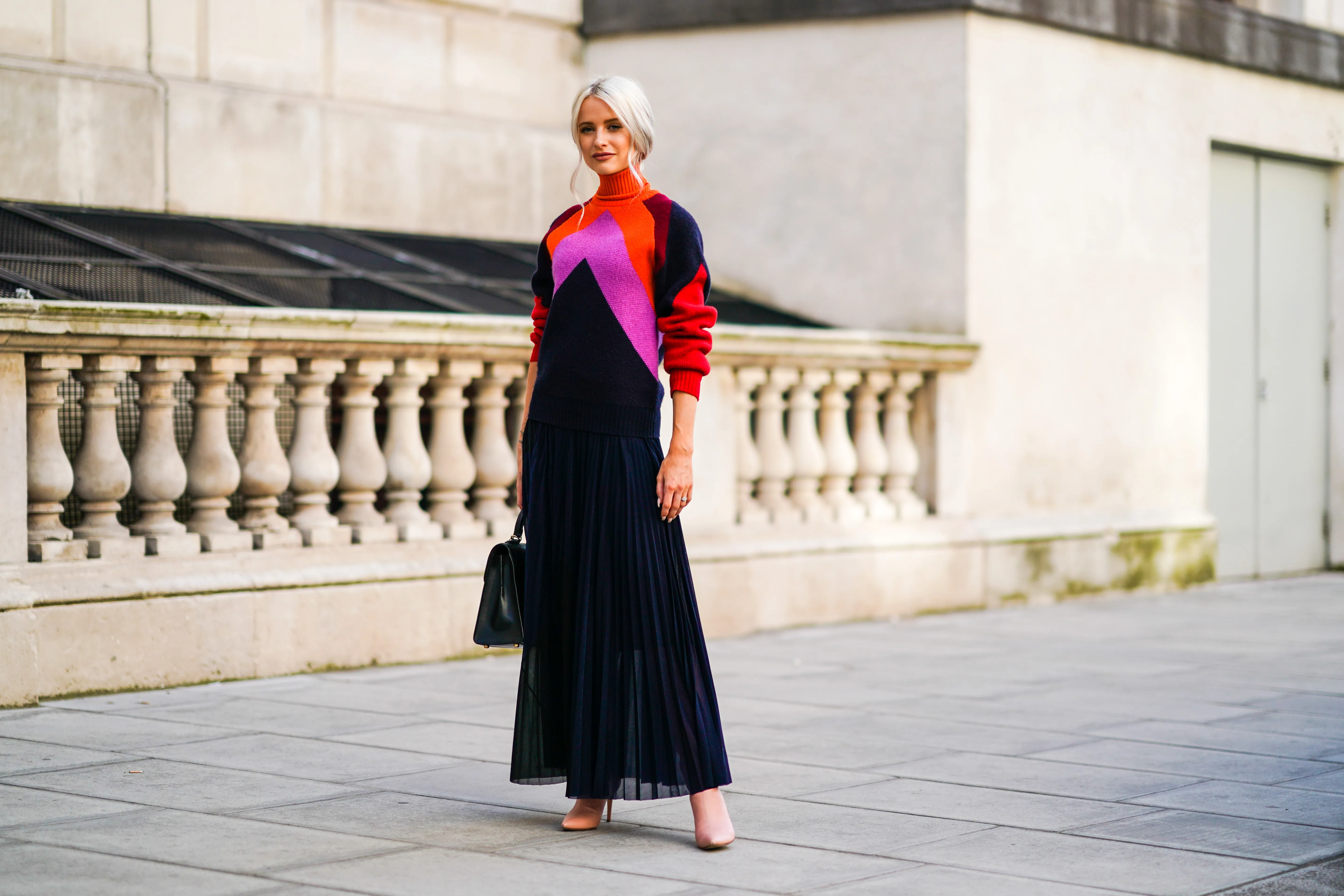 Victoria Magrath wears an orange red and pink wool pullover with a turtleneck, a black lace pleated skirt, a black leather bag, during London Fashion Week September 2019 on September 15, 2019 in London, England.