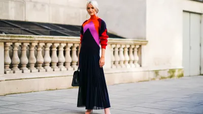 Victoria Magrath wears an orange red and pink wool pullover with a turtleneck, a black lace pleated skirt, a black leather bag, during London Fashion Week September 2019 on September 15, 2019 in London, England.