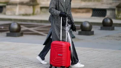 PARIS, FRANCE - JANUARY 17: A passerby wears a white woven turtleneck wool pullover, a gray oversized long coat, black denim jeans ripped pants, white leather laces sneakers, black shiny leather gloves, a black shiny leather crossbody bag, a transparent umbrella, a red large suitcase, on January 17, 2021 in Paris, France. (Photo by Edward Berthelot/Getty Images)